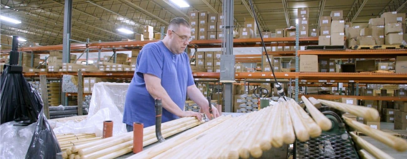 1 An man in a purple shirt works in a warehouse stacking brooms
