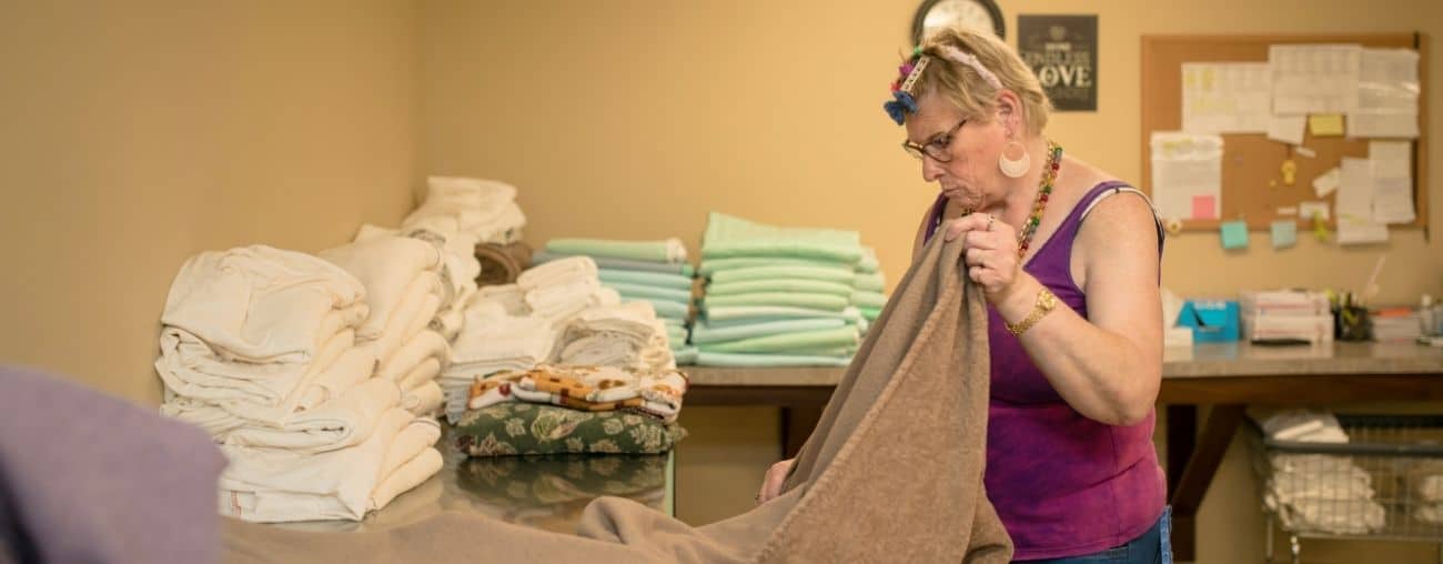 A woman in a purple shirt and glasses is seen folding blankets at a work site.