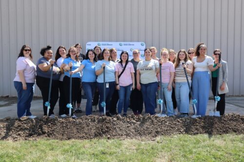 Group holding shovels at a groundbreaking ceremony outside a building