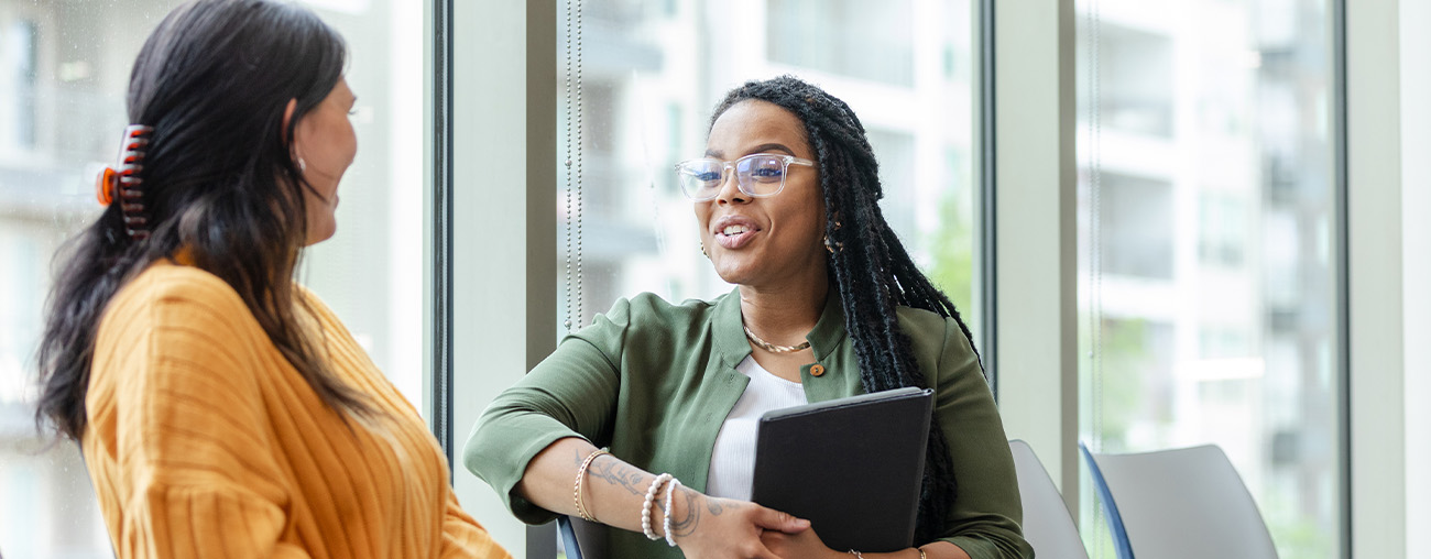 Two women talking in front of a row of windows