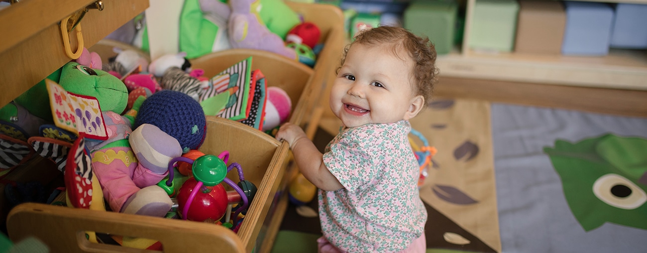A baby smiling while holding on to a toy bin.