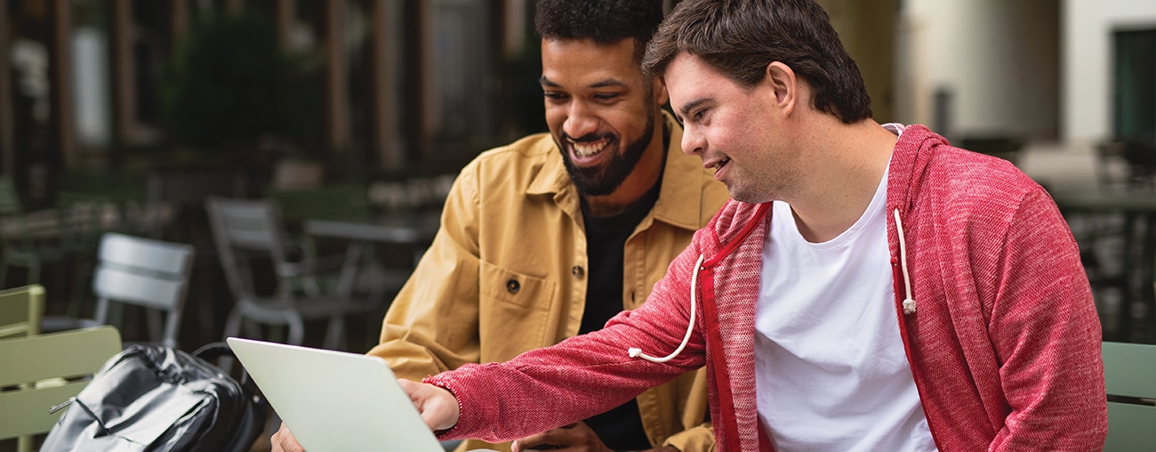 Two friends working on a computer outside on a picnic table