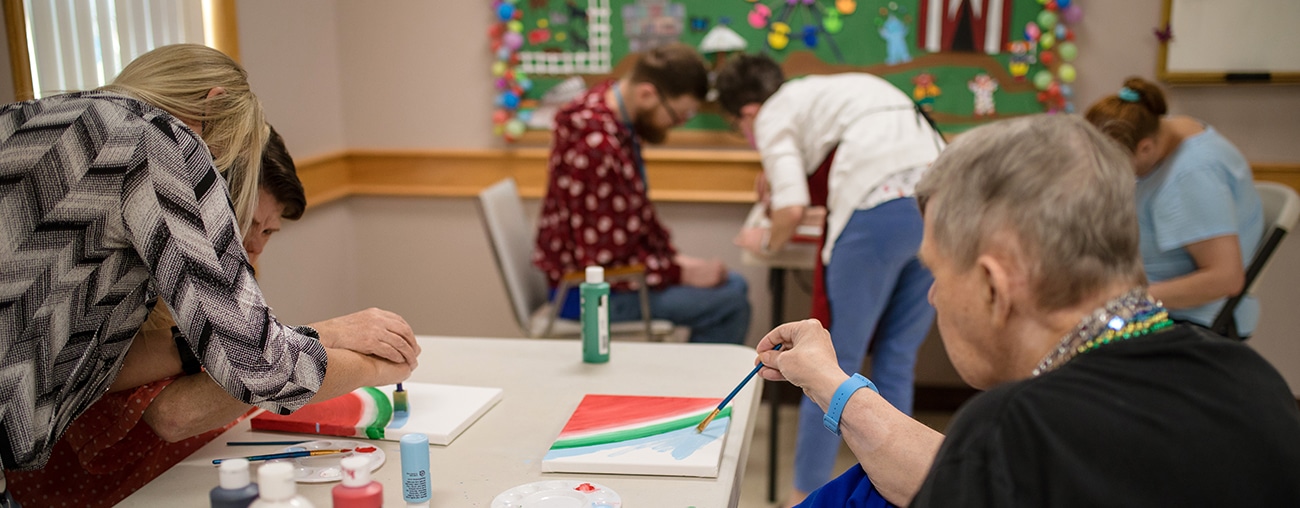 A group of people painting on canvases with some volunteers helping.