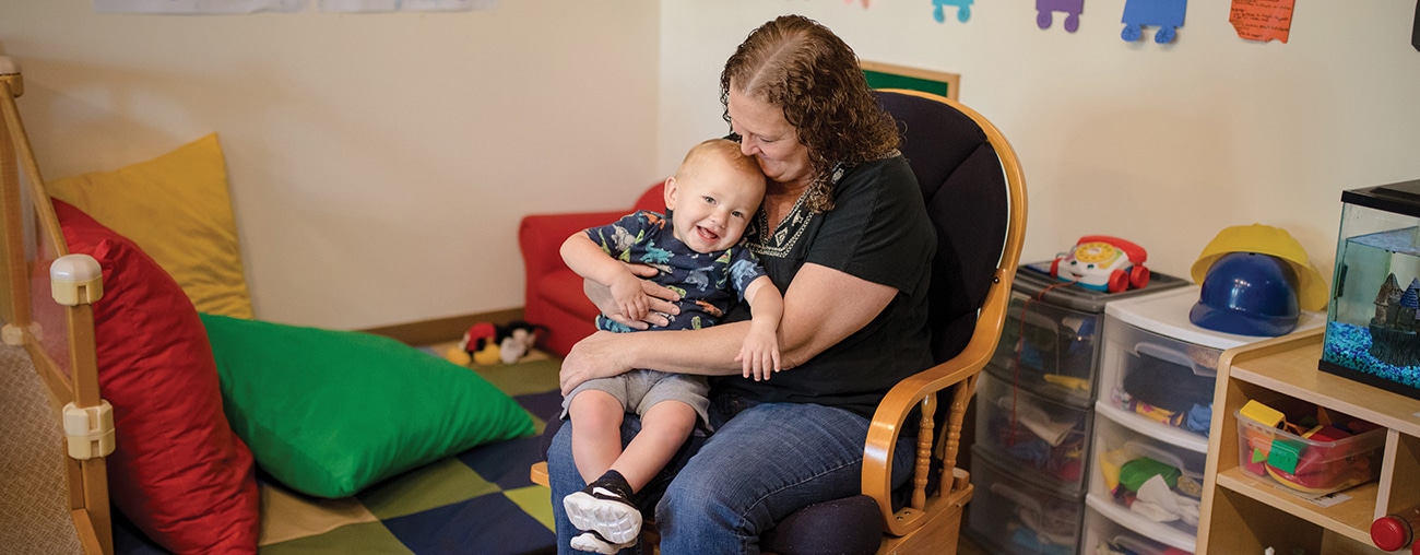 A smiling woman in a rocking chair with a happy young child sitting on her lap.