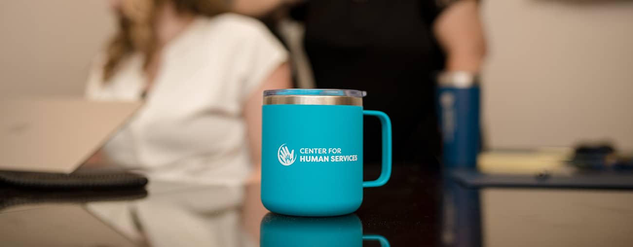 A teal CHS logo travel mug on a table