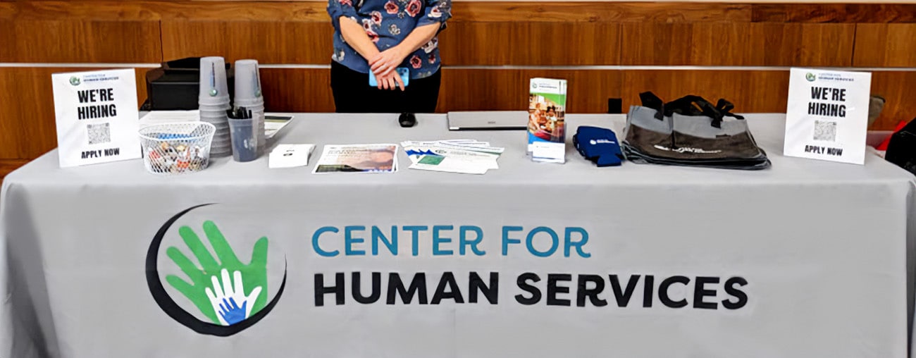 A Center for Human Services booth at a community event with informational materials spread across a table