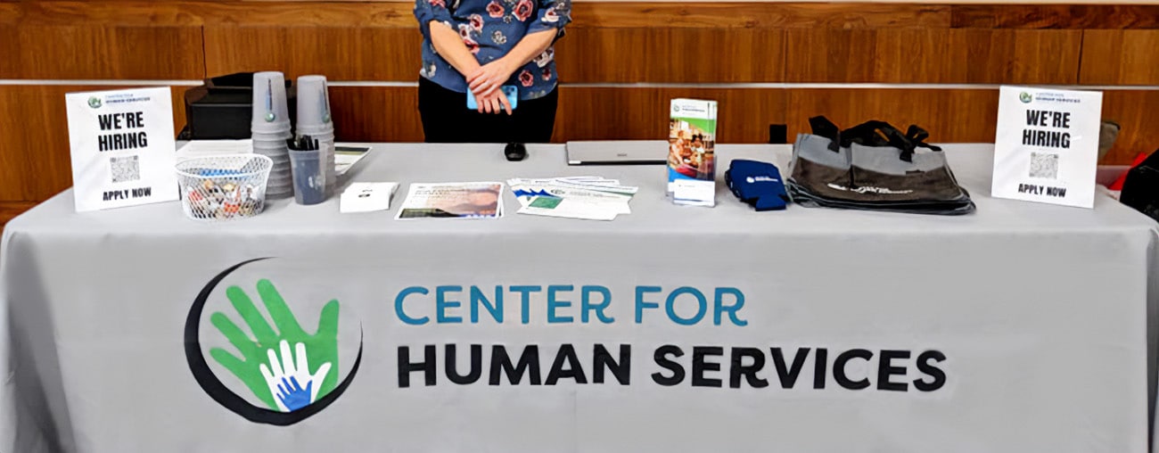 make-an-impact-business-partners-v2 A Center for Human Services booth at a community event with informational materials spread across a table