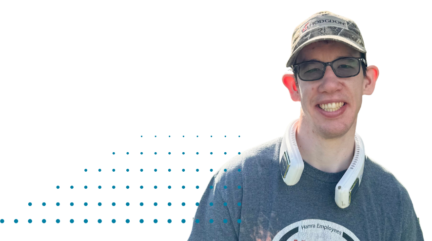 A teenager wearing a hat and sunglasses smiles at the camera