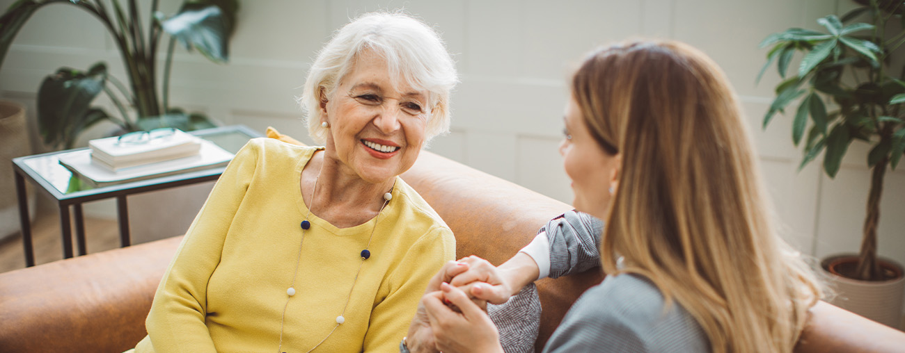 A senior woman and young adult woman talking on a couch